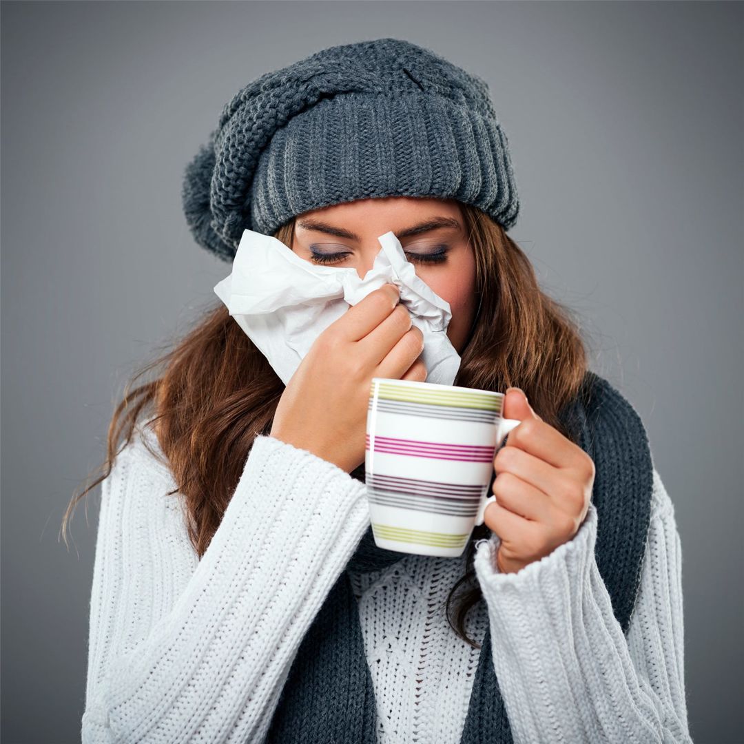 Woman with a cold holding a tissue and a warm drink